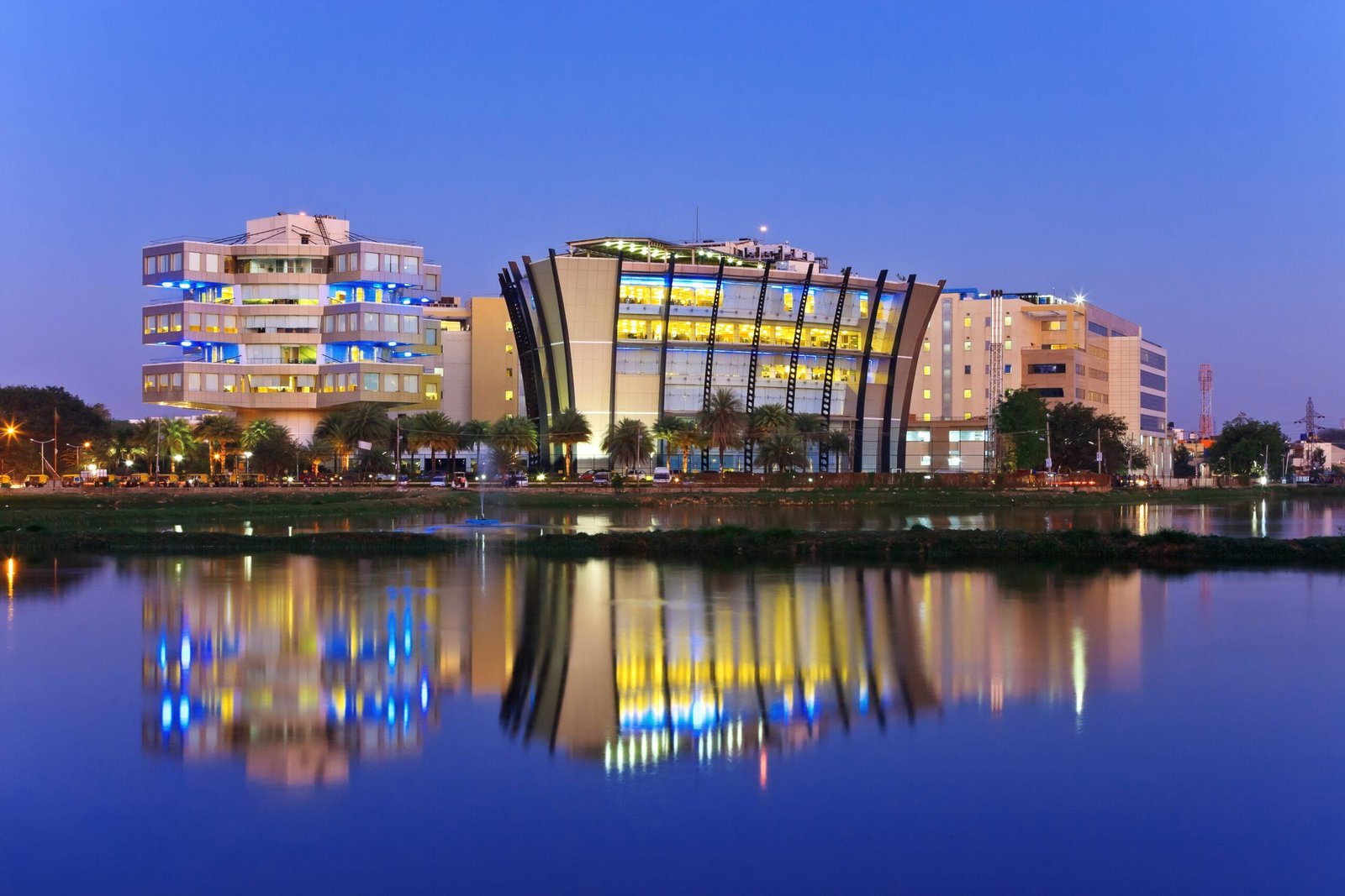 Modern office buildings in Bengaluru reflected in a lake at dusk.